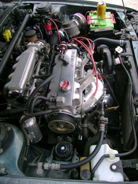 1989 Mazda MX-6 - The engine bay shows a 12-valve engine with various aftermarket modifications and a soda can resting on the battery.