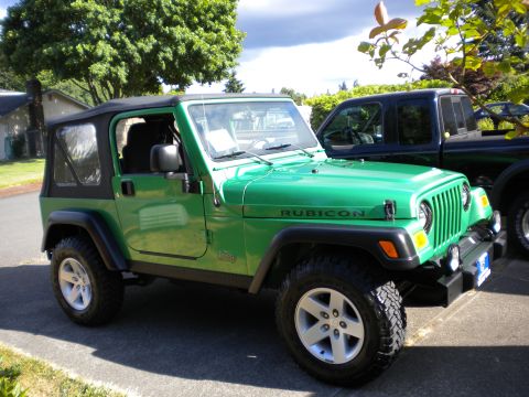 1986 Ford Bronco - Green Jeep Wrangler Rubicon is parked next to a dark pickup truck.