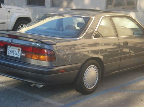 1989 Mazda MX-6 - A gray Mazda MX-6 is parked next to a white SUV, showing its rear quarter panel and spoiler.