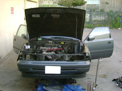 1989 Mazda MX-6 - The engine bay of a gray coupe is exposed with the hood and driver's side door open.