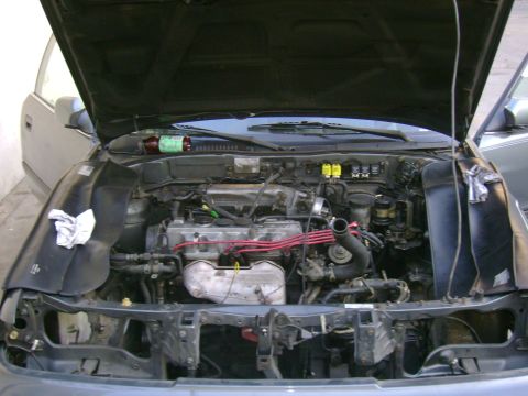 1989 Mazda MX-6 - The engine compartment of a car is open for inspection, revealing the mechanical workings within.