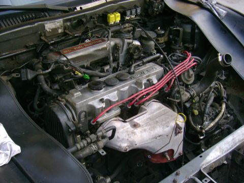 1989 Mazda MX-6 - The engine bay of a car, showing the V6 engine with fuel injection and red spark plug wires.