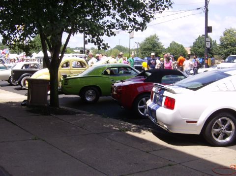 1970 Ford Ranchero - Several cars are parked along a sidewalk at a car show, with spectators in the background.