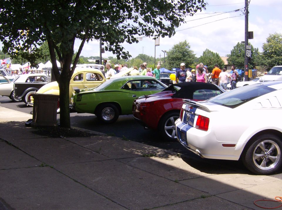 Cars parked in a line at an outdoor event, with people milling around