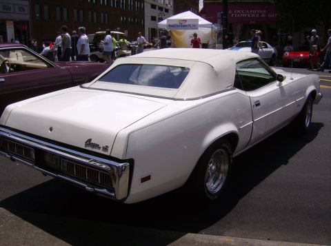 1970 Ford Ranchero - A white convertible with a tan top is parked at a car show, with other vehicles and people in the background.