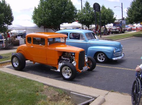 1970 Ford Ranchero - Two vintage cars, an orange hot rod and a blue sedan, are parked together at a car show.