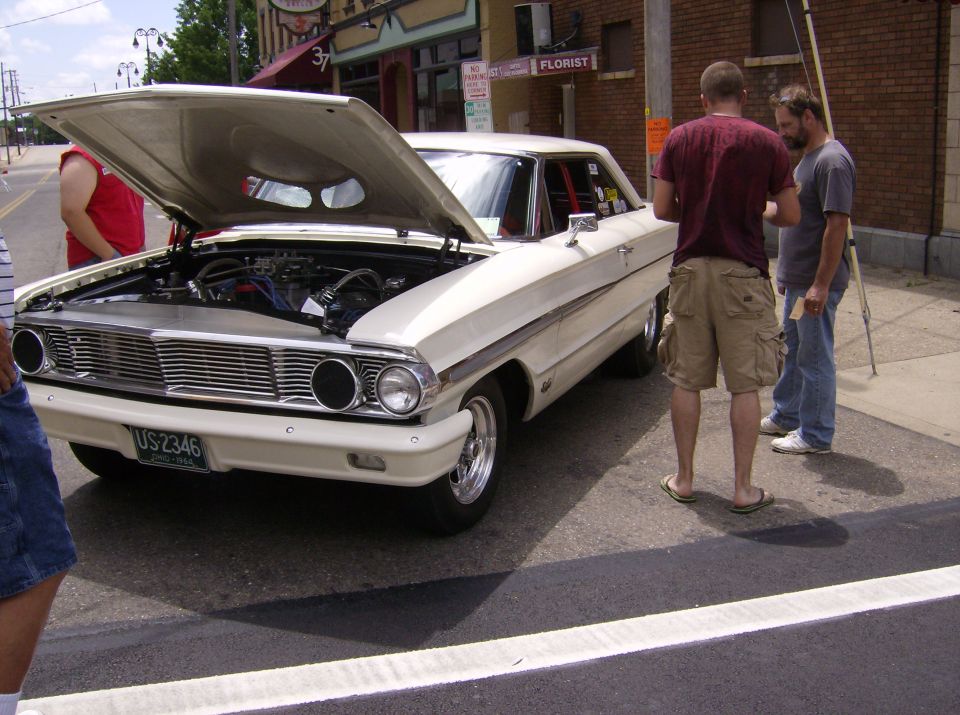 White 1964 Ford Galaxie 500 with hood open, showing engine. Two guys stand nearby