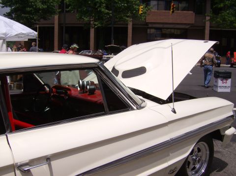 1970 Ford Ranchero - A white classic car with its hood open and a glimpse of its red interior is on display at an outdoor event.