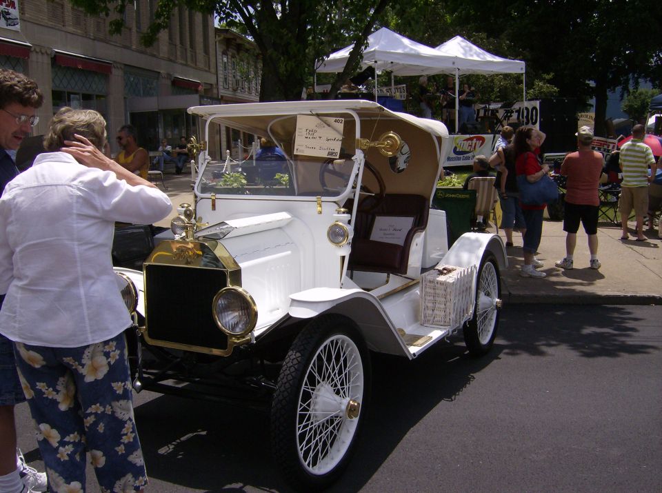 White antique car with a wicker basket on the side, viewed from the front-right