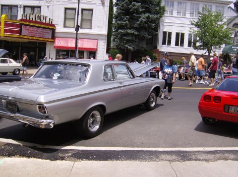 1970 Ford Ranchero - A silver 1964 Plymouth Belvedere coupe is parked on a street with its hood up, alongside other vehicles and spectators.