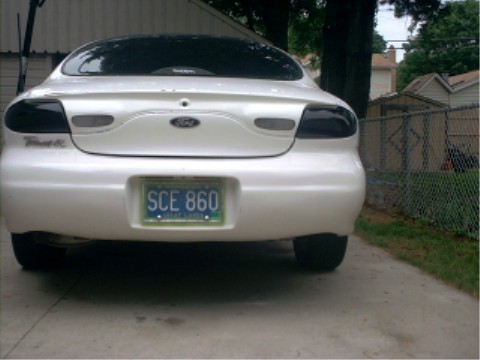 1997 Ford Taurus - White 1997 Ford Taurus sedan parked in a driveway, showing its rear end and license plate.