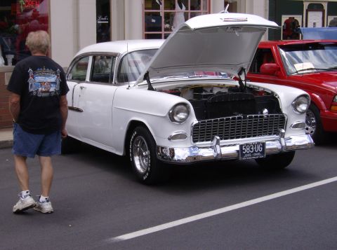 1970 Ford Ranchero - A white 1955 Chevrolet sedan is displayed with its hood open, parked next to a red vehicle.