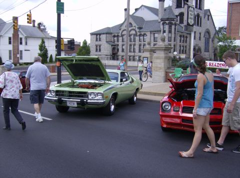 1970 Ford Ranchero - A light green coupe with its hood open is parked on a street next to a red car.