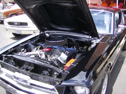 1970 Ford Ranchero - A black 1969 Ford Mustang is displayed with its hood open, revealing the engine bay. Another vehicle is visible behind it.