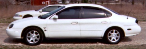 1997 Ford Taurus - A white 1997 Ford Taurus is seen from the side, parked outdoors next to another vehicle.