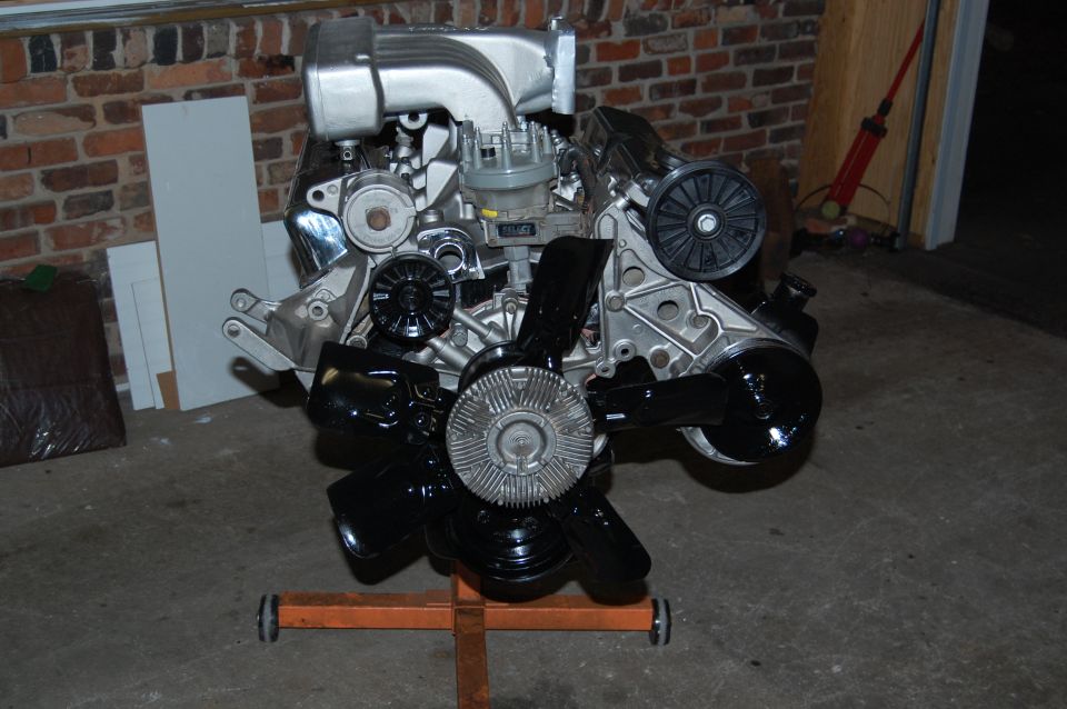 V8 engine on an orange engine stand, with brick wall and garage door in background