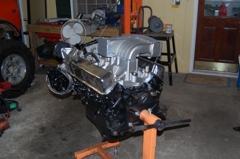 1994 Ford Bronco - Engine assembly on a stand in a garage, with a tire and part of a vehicle in the background.