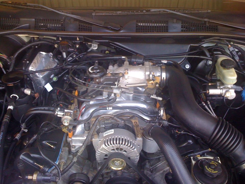 Engine bay of 1999 Mercury Grand Marquis showing V8 intake manifold, alternator, and black air intake tube