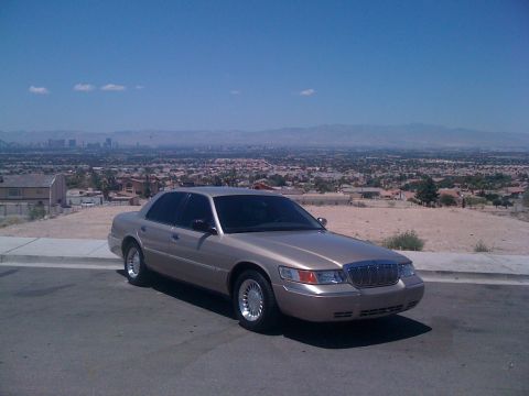 1999 Mercury Grand Marquis - A gold Mercury Grand Marquis sedan is parked on a street overlooking a city.