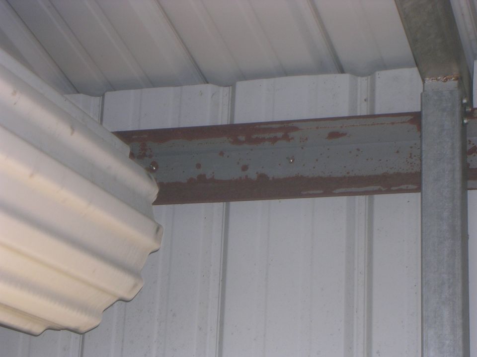 Rusty steel girt and galvanized post inside a white metal building