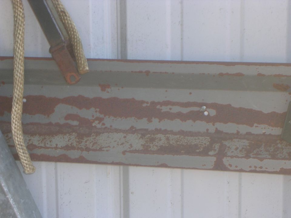 Rusty olive-grey steel beam against white corrugated metal wall with rope hanging