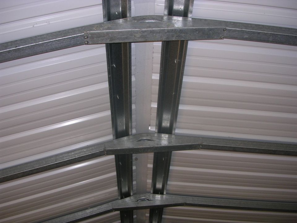 Galvanized steel trusses under the white ribbed roof of a metal carport building