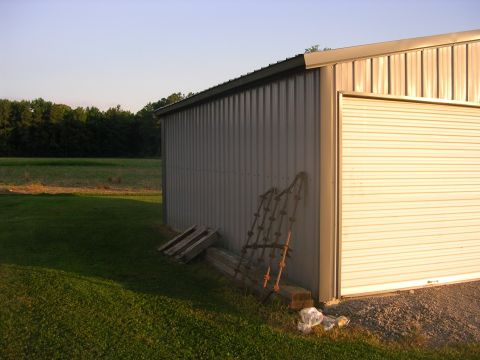 2008 Bombardier Outlander - A metal shed with a roll-up door sits beside a grassy field, with old farm equipment leaning against its wall.
