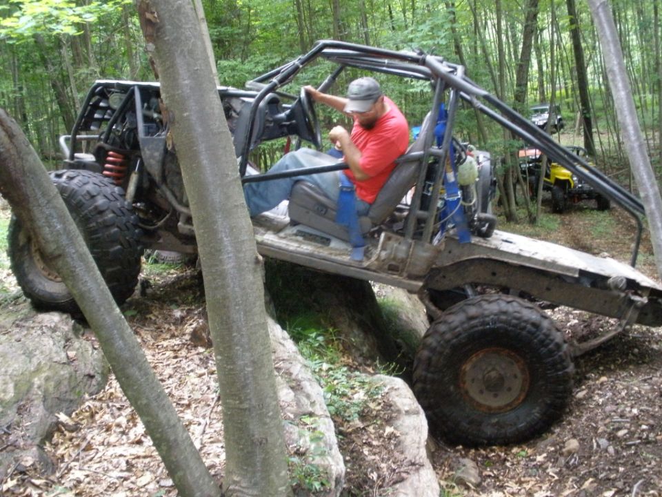 Off-road buggy with roll cage, large tires, and a driver in a red shirt navigating rocks