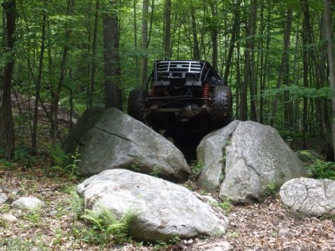 1995 Ford Bronco - This heavily modified off-road vehicle is shown navigating a rocky trail in a wooded area.
