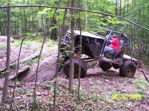 1995 Ford Bronco - An off-road buggy is driven through a wooded area with large rocks.