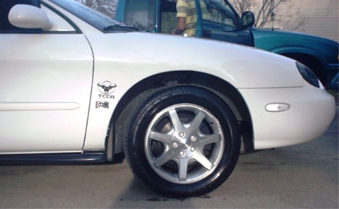 1997 Ford Taurus - A white sedan is parked next to other vehicles, a bull decal on its front fender.