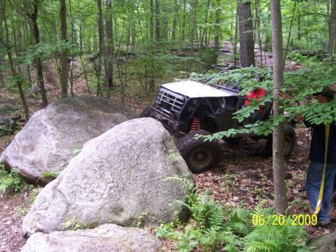 1995 Ford Bronco - A custom off-road buggy attempts to maneuver through a rocky trail in a forest setting.
