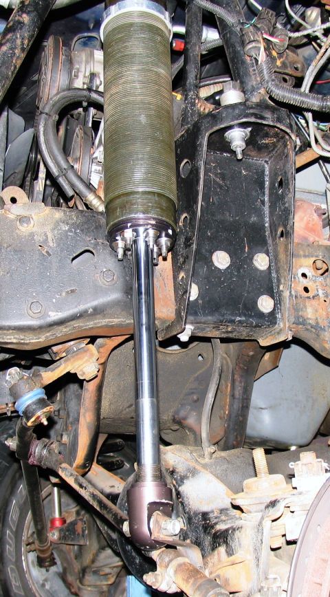 1984 Ford Bronco - Close-up view of aftermarket front suspension components, including a large shock absorber and associated hardware.