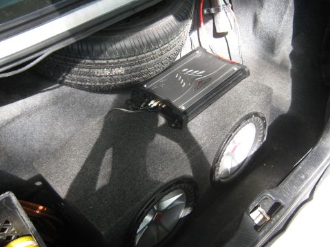 1997 Ford Crown Victoria - The trunk of a car shows a spare tire, an audio amplifier, and two subwoofers.