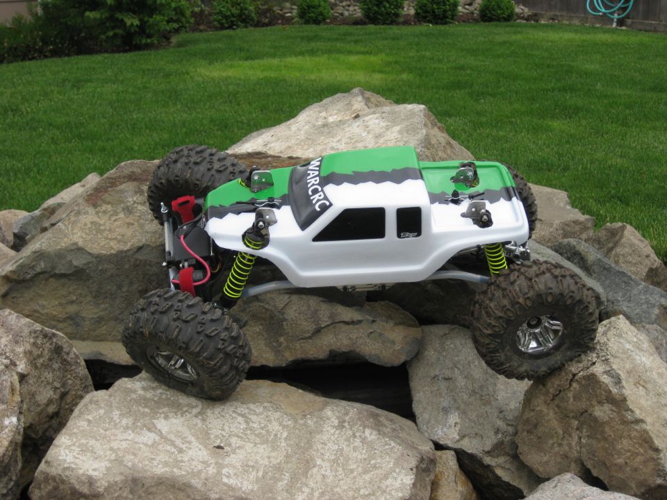 RC rock crawler with green and white body on rocks. Text 'WARCRC' visible on the roof