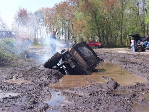 2005 Ford Excursion - An off-road vehicle is stuck in a deep mud pit, with smoke billowing from its engine compartment.
