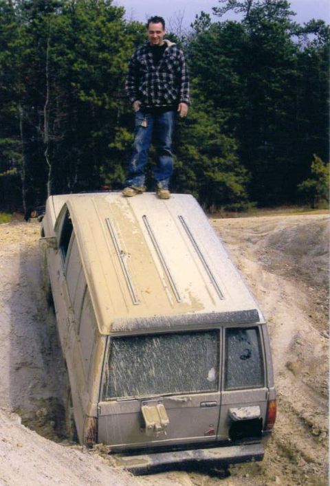 2005 Ford Excursion - A man stands atop a tan 2005 Ford Excursion that is stuck in a dirt ditch.
