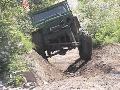 1992 Ford Bronco - A stripped, green-painted open-top 4x4 with an exposed tube roll cage leans hard while crawling down a rutted dirt bank on an off-road trai…