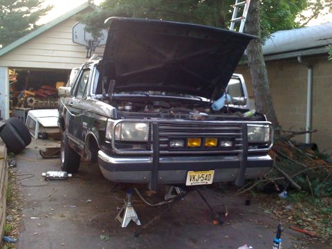 1988 Ford Bronco - Ford Bronco's hood is open while it's on jack stands in a driveway.