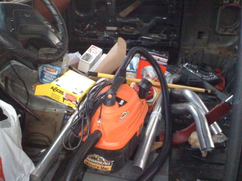 1988 Ford Bronco - The interior of a vehicle is cluttered with various items, including a shop vac and exhaust pipes.