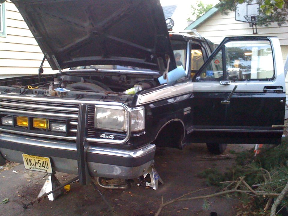 1988 Ford Bronco front end with hood open, driver door ajar, on jack stands