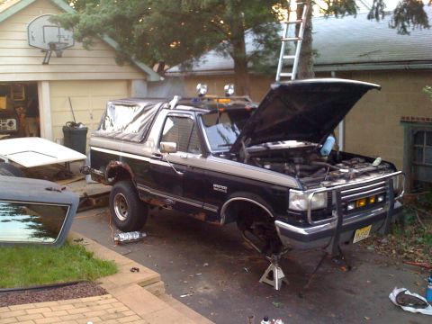 1988 Ford Bronco - Ford Bronco undergoing maintenance with the hood up and front end raised on jack stands.