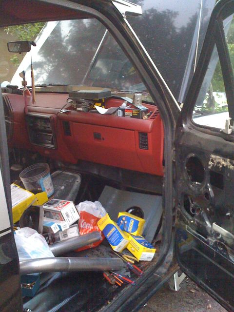 1988 Ford Bronco - The interior of a vehicle is cluttered with parts and tools, with the hood open.