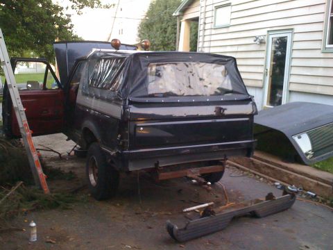 1988 Ford Bronco - A black SUV with a soft top is parked in a driveway, undergoing repairs.