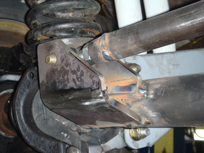 Custom fabricated suspension bracket welded to a metal tube, with a coil spring visible above