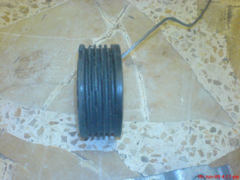 1992 Ford Crown Victoria - A disassembled window motor pulley with a cable attached lies on a terrazzo floor.