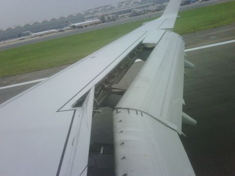 1996 Ford Bronco - View from an airplane window shows the wing and flaps extended on the tarmac, with airport buildings and planes visible.
