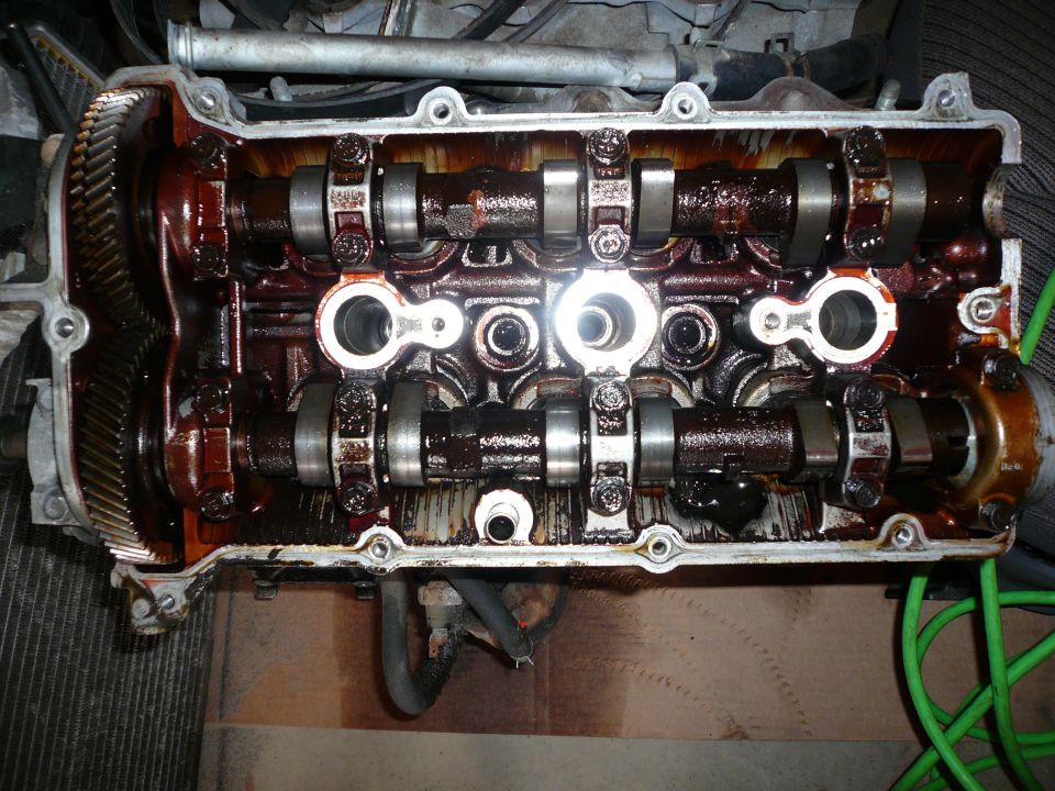 Engine valve cover removed, showing camshafts and oily internal components