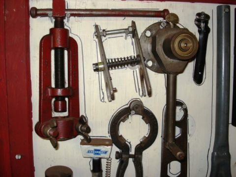 1909 Ford Model T - Vintage automotive tools, including a red screw clamp and a Chevrolet emblem, are organized on a wooden board.