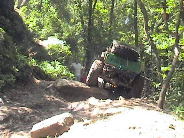 Green off-road vehicle with spare tires on top navigating a dirt trail